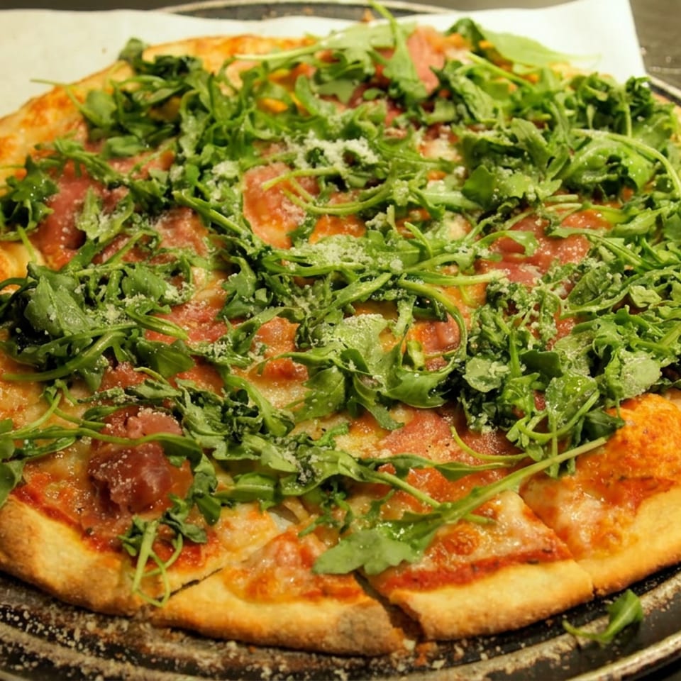 Round thin-crust pizza topped with melted cheese, tomato sauce, fresh arugula, and grated cheese on a dark plate.