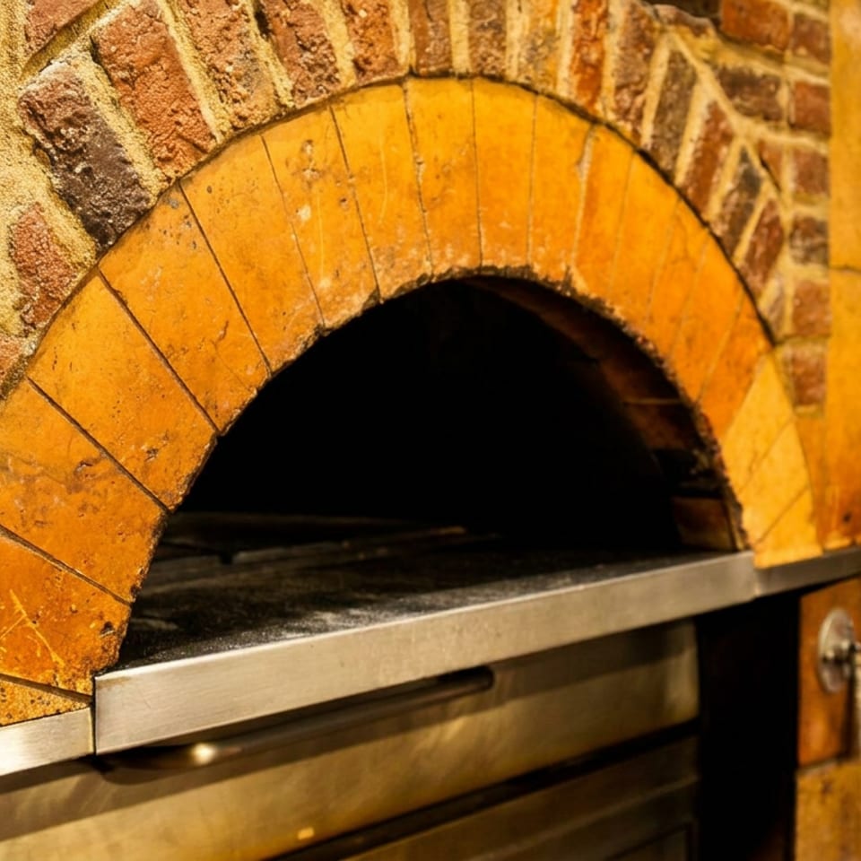 Brick-arched wood-fired oven with a dark baking chamber and stainless-steel hearth in a restaurant kitchen.