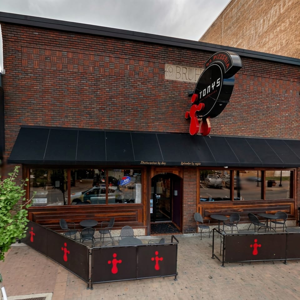 Brick restaurant storefront with outdoor patio seating, black awning, and prominent circular Torchy’s Tacos sign.