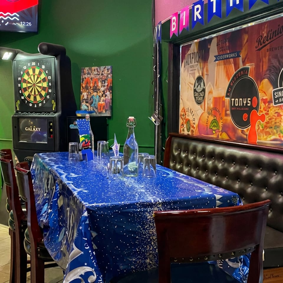 Restaurant dining area decorated with blue and silver balloons, a starry tablecloth, glassware, dartboard, and brewery mural.