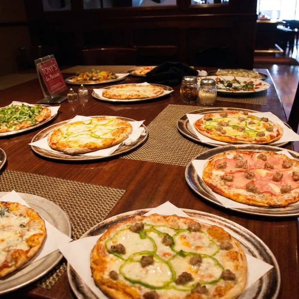 Restaurant table covered with assorted pizzas featuring vegetables, meats, and cheeses in a warmly lit dining room.